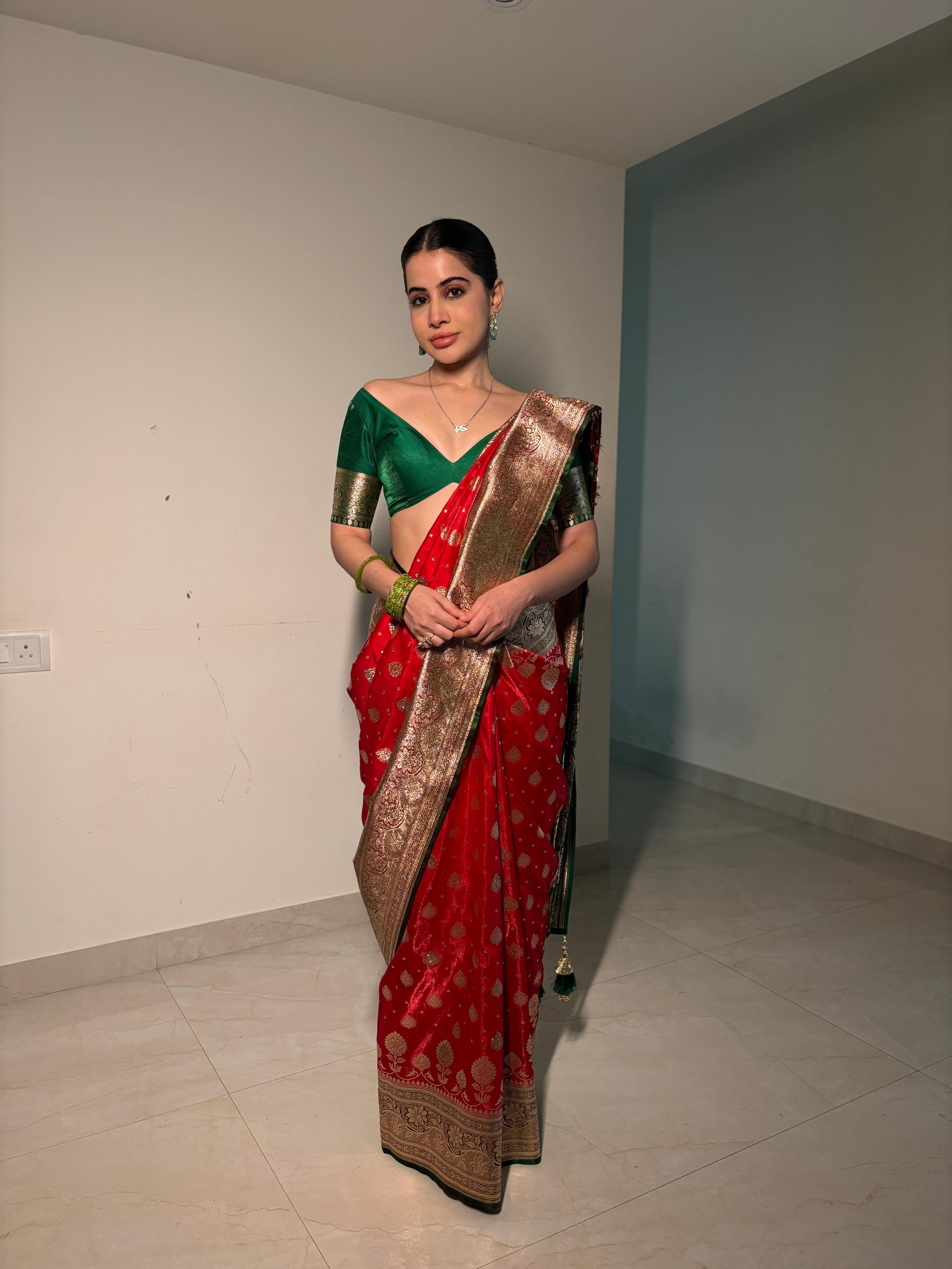 Woman wearing a red and green saree with a gold border in an indoor setting.